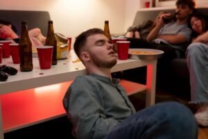A young man resting his head against a white table full of red cups.