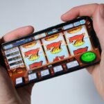 A person holds a smartphone displaying a slot machine game, depicting the dangers of online casinos.