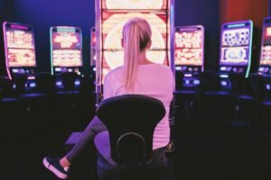 A person sits in front of a brightly lit slot machine in a dark casino.