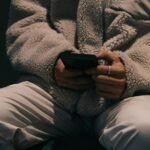 A person sits in a dimly lit setting, holding a smartphone with both hands, depicting safe online gambling.