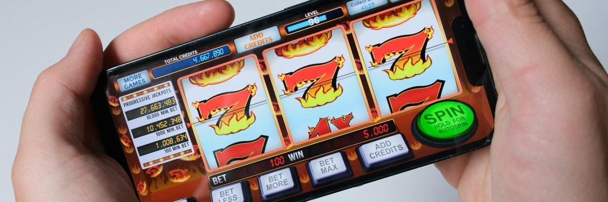 A person holds a smartphone displaying a slot machine game, depicting the dangers of online casinos.