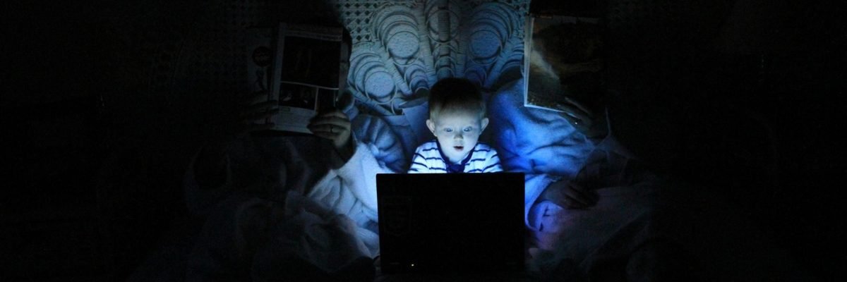 Child illuminated by a laptop's blue light in a dark room, conveying how online gambling addiction is rising.