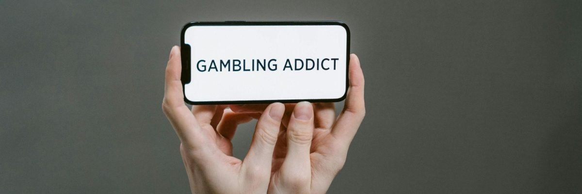 Hands bound in chains hold a phone with "GAMBLING ADDICT" displayed, conveying why internet gambling can be more dangerous.