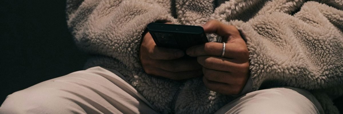 A person sits in a dimly lit setting, holding a smartphone with both hands, depicting safe online gambling.
